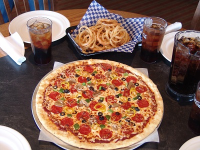 Table with soft drinks, onion rings, and specialty pepperoni pizza